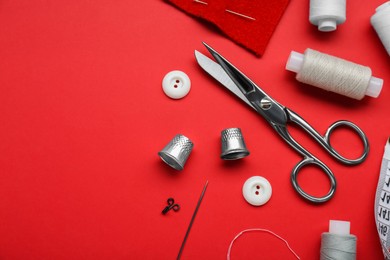 Photo of Flat lay composition with thimbles and different sewing tools on red background. Space for text