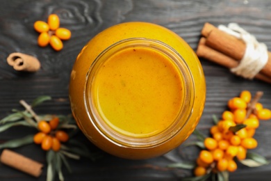 Delicious sea buckthorn jam and fresh berries on black wooden table, flat lay