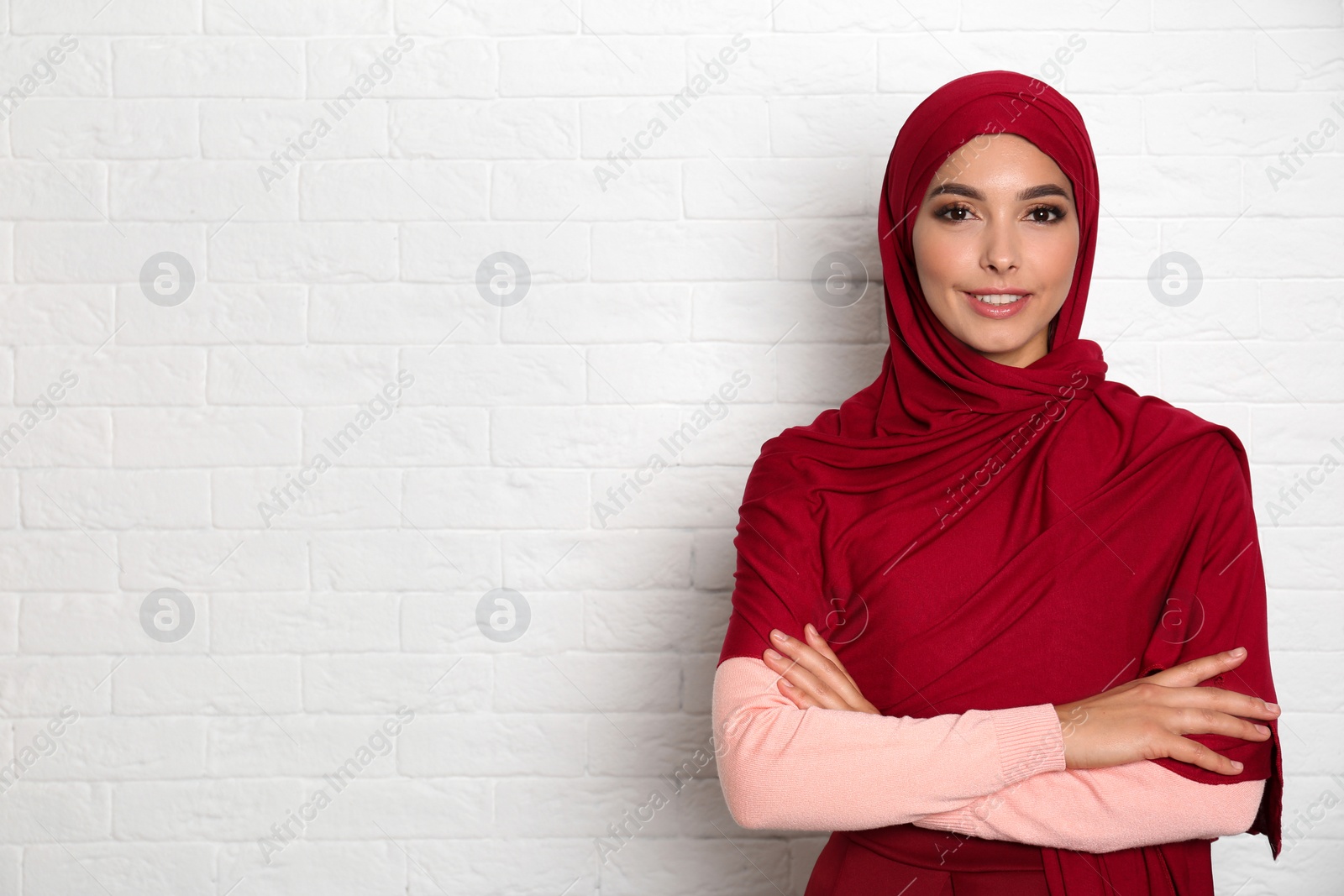 Photo of Portrait of young Muslim woman in hijab against brick wall. Space for text