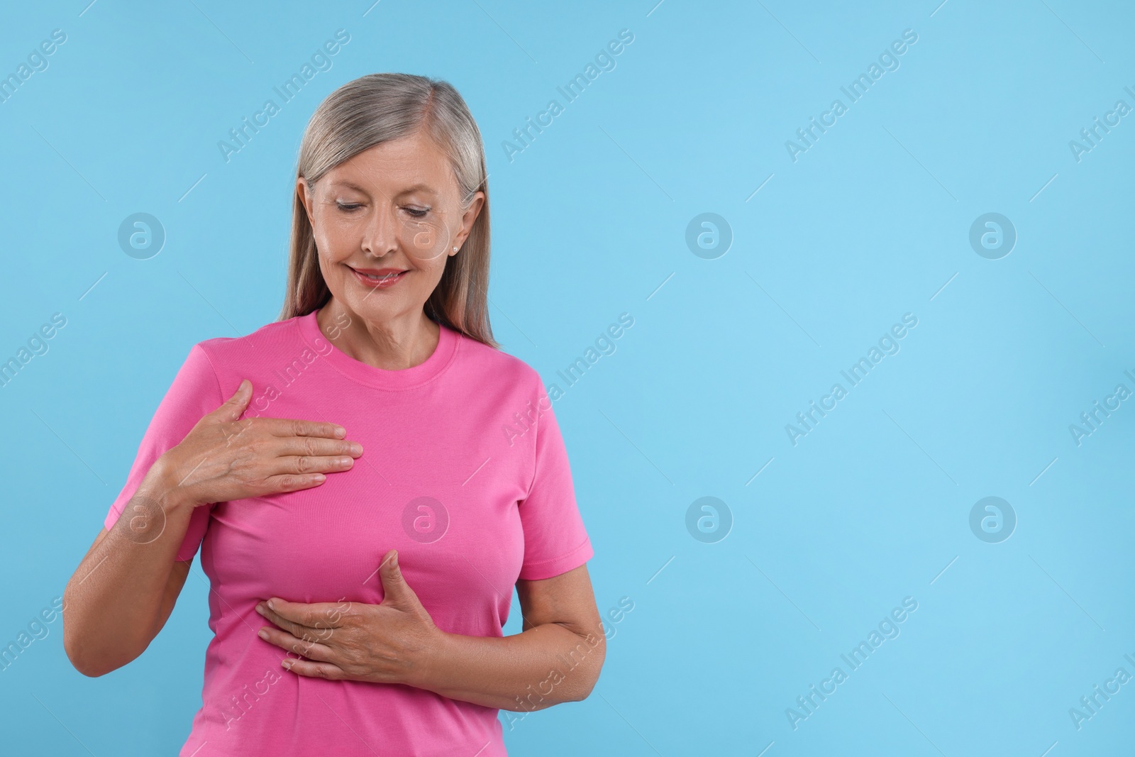 Photo of Beautiful senior woman doing breast self-examination on light blue background, space for text