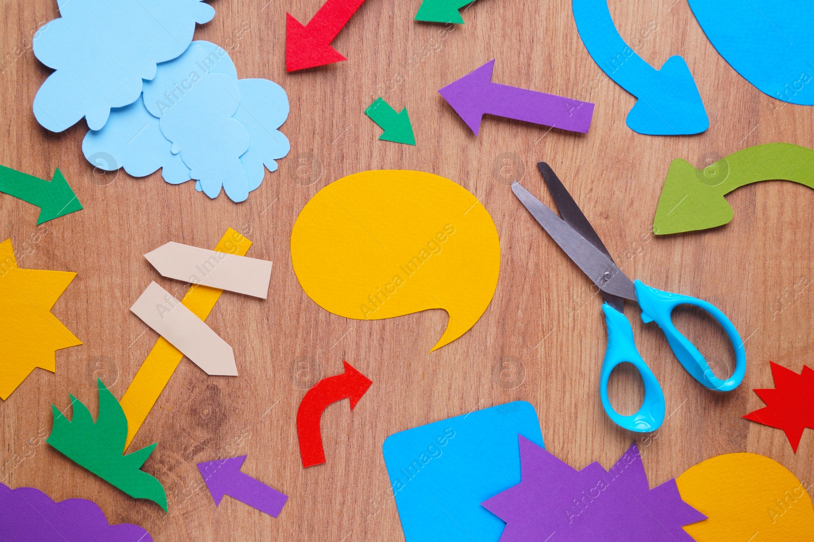 Photo of Scissors and different paper figures on wooden table, flat lay. Space for text