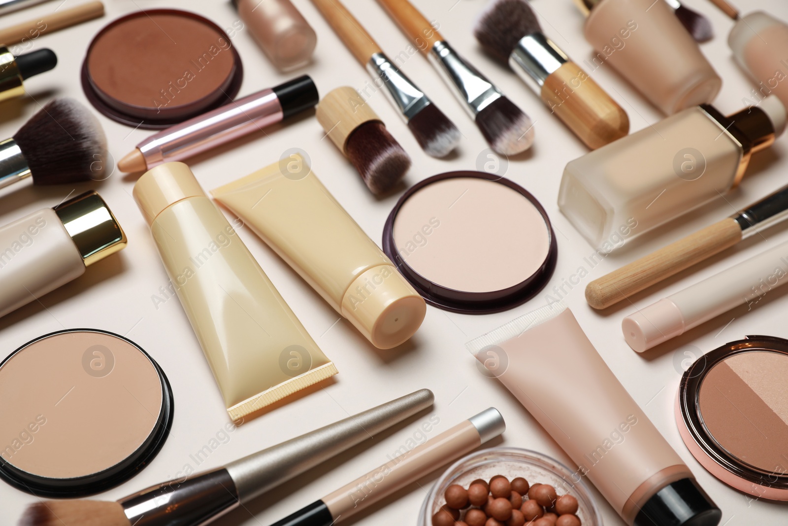 Photo of Face powders and other makeup products on beige background, closeup