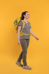Photo of Smiling young woman with backpack walking on orange background. Active tourism