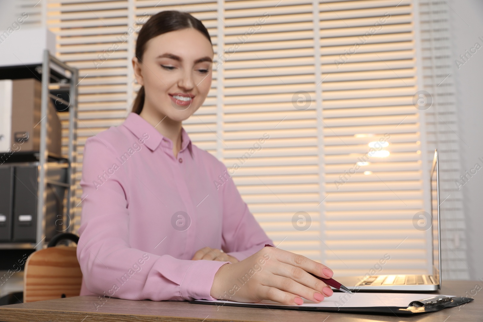 Photo of Happy woman taking notes at wooden table in office, selective focus. Space for text