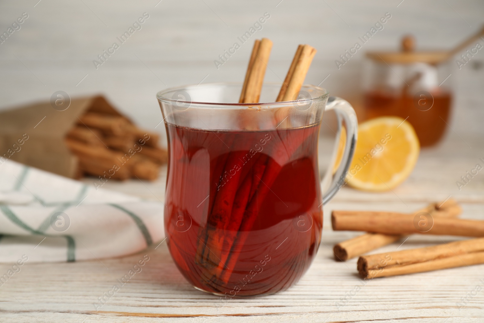 Photo of Glass cup of hot tea with aromatic cinnamon on white wooden table, closeup