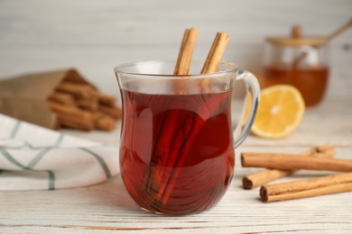 Glass cup of hot tea with aromatic cinnamon on white wooden table, closeup