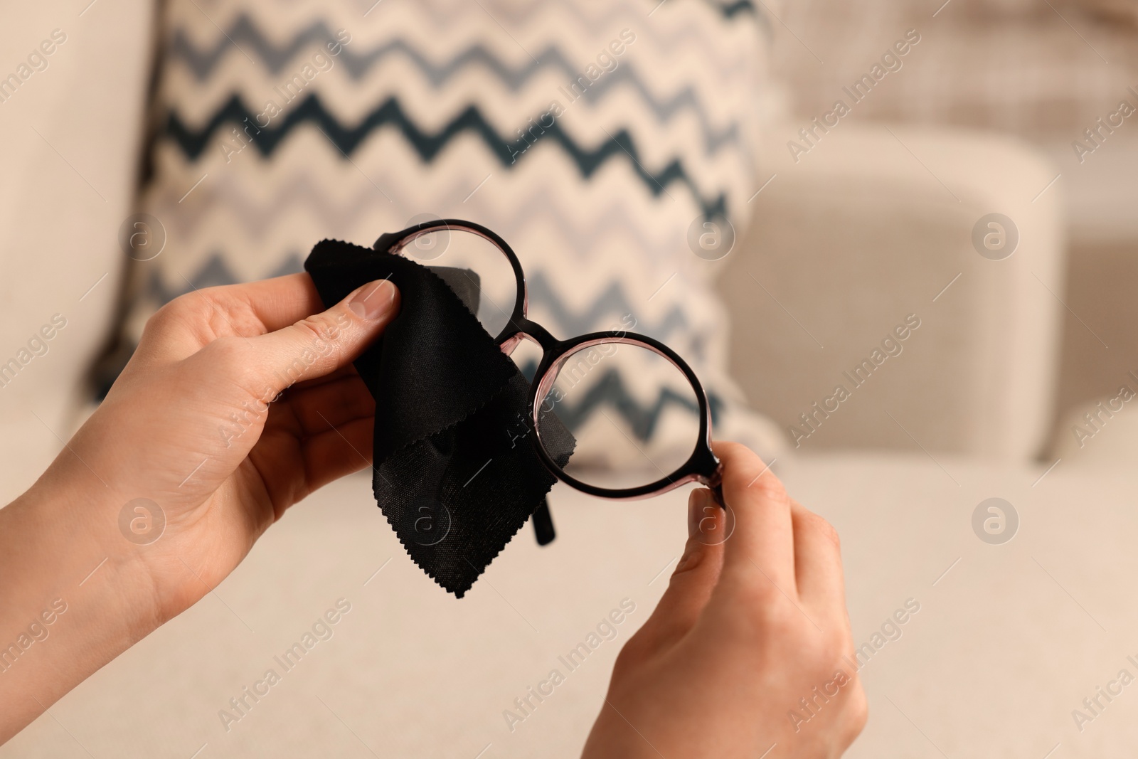 Photo of Woman cleaning glasses with microfiber cloth at home, closeup