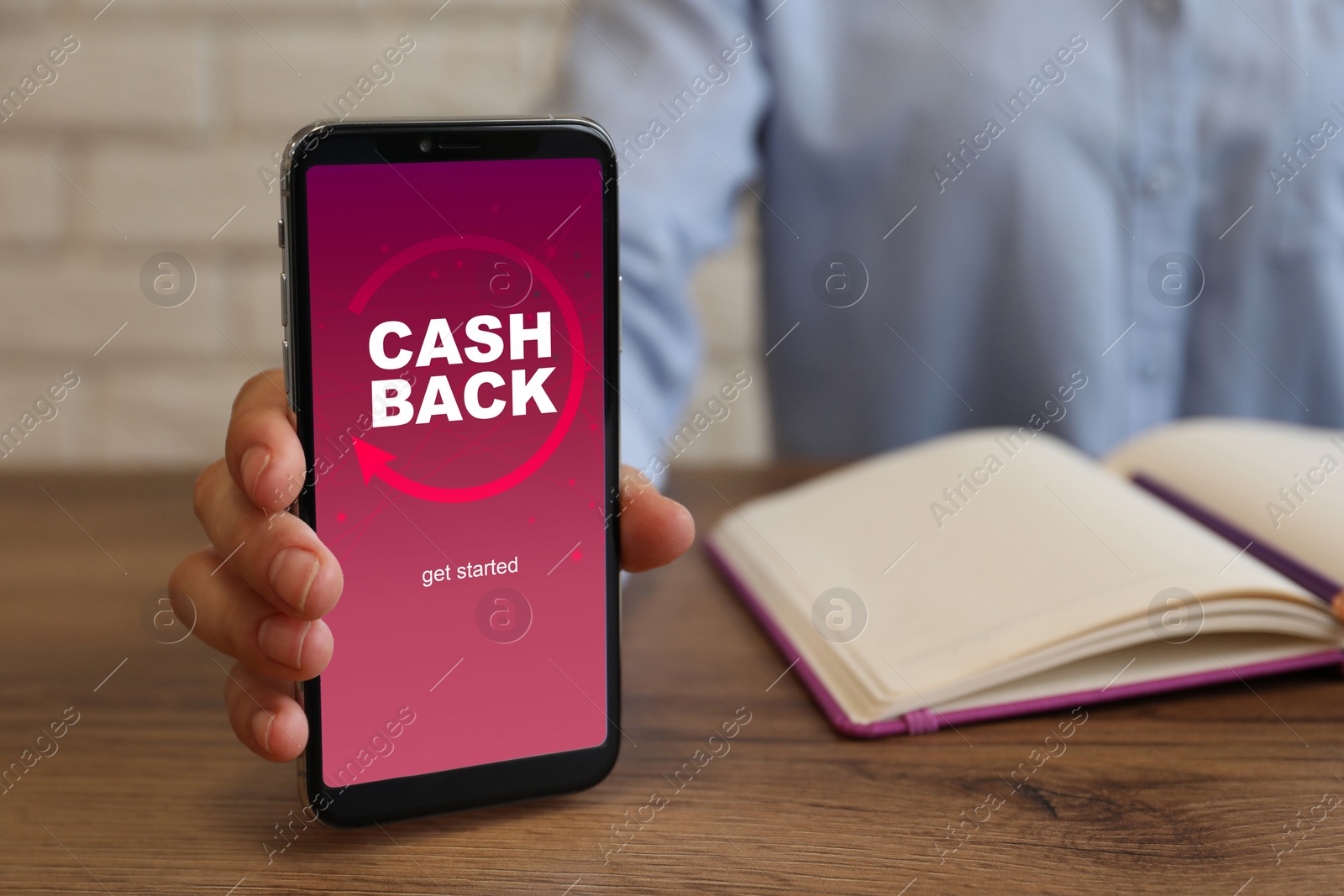 Image of Woman holding smartphone with word Cashback at wooden table, closeup