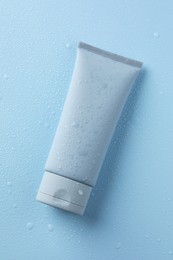 Moisturizing cream in tube on light blue background with water drops, top view