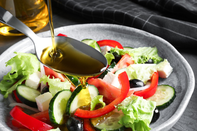 Adding cooking oil to delicious salad on table, closeup