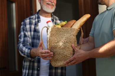 Photo of Man with bag of products helping his senior neighbour outdoors, closeup