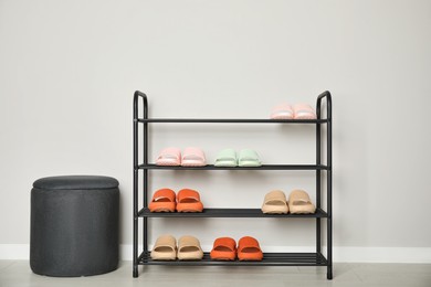 Photo of Shoe rack with different pairs of rubber slippers near white wall indoors