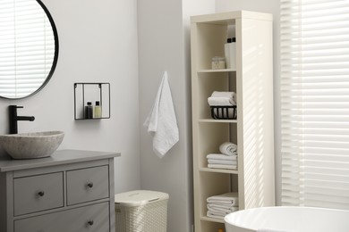 Stylish bathroom interior with grey chest of drawers and shelving unit