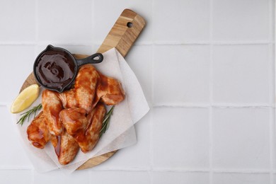 Photo of Raw chicken wings, rosemary, lemon and marinade on light tiled table, top view. Space for text