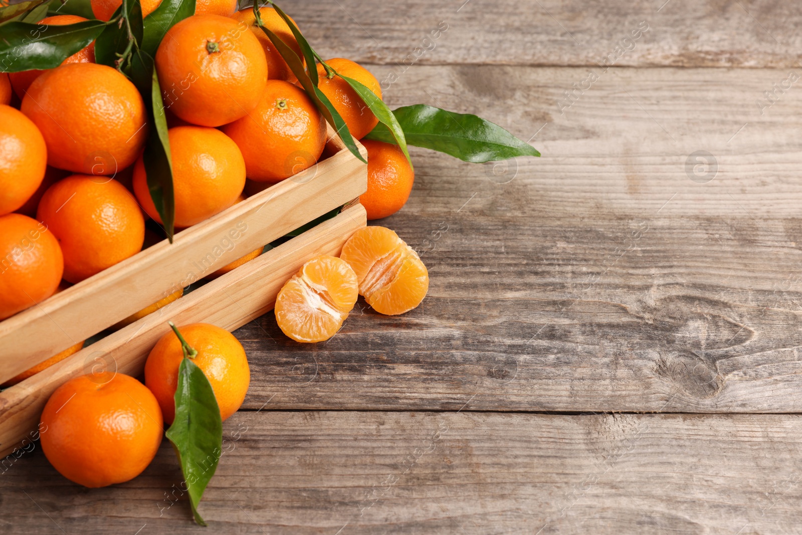 Photo of Delicious tangerines with leaves on wooden table. Space for text