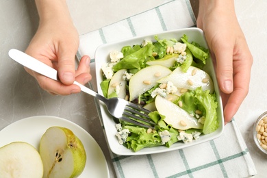Photo of Woman eating fresh salad with pear at light table, top view