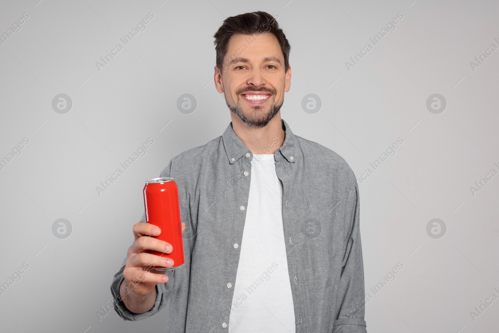 Photo of Happy man holding red tin can with beverage on light grey background