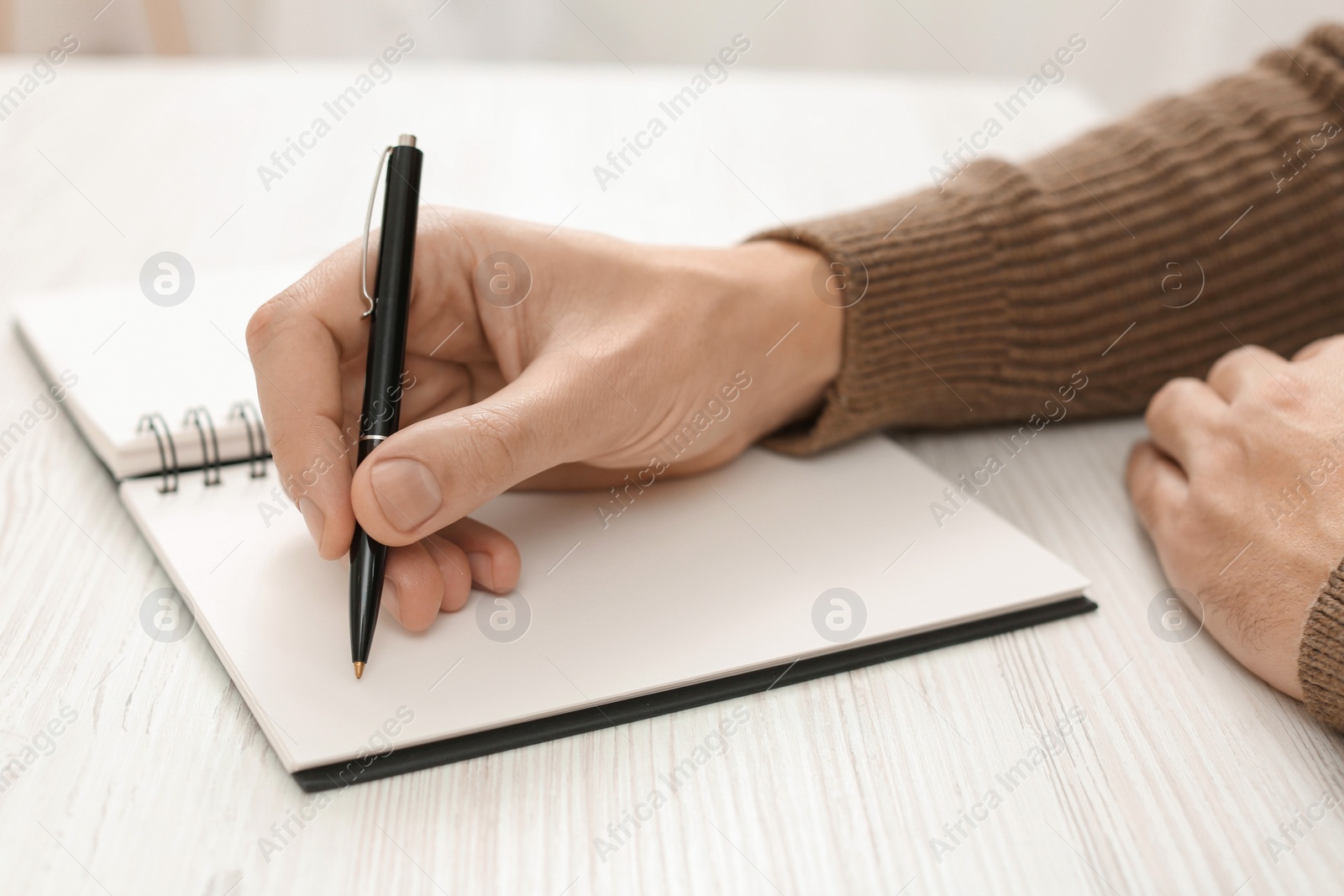 Photo of Man writing in notebook at white wooden table, closeup