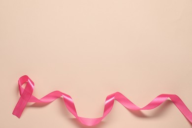 Breast cancer awareness. Pink ribbon on beige background, top view. Space for text