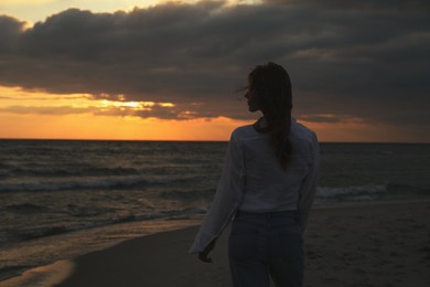 Woman on sandy beach during sunset, back view