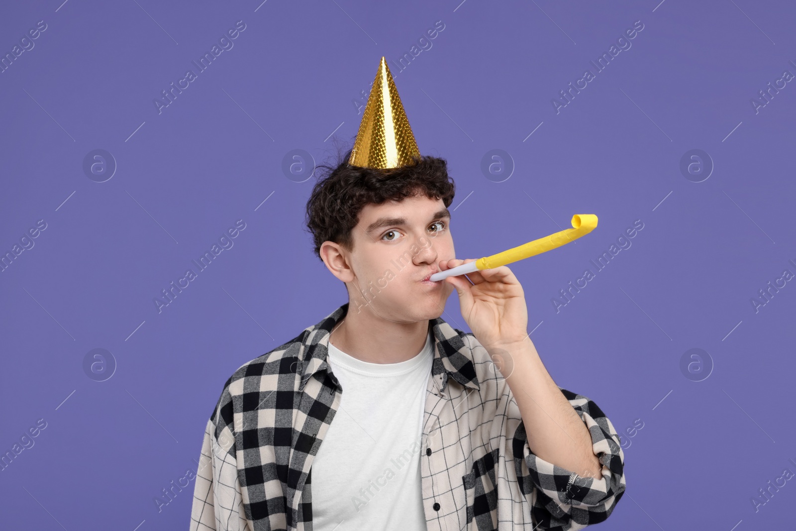 Photo of Young man in party hat with blower on purple background