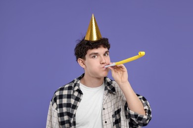 Young man in party hat with blower on purple background