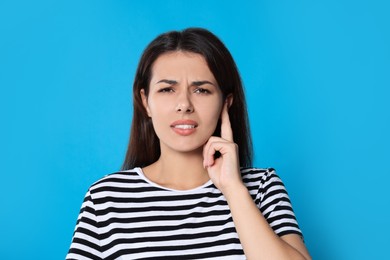 Young woman suffering from ear pain on light blue background