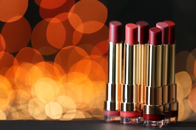 Photo of Set of bright lipsticks on table against blurred lights, space for text