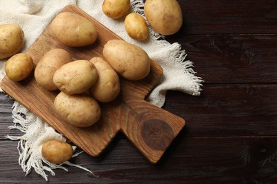 Photo of Raw fresh potatoes and cutting board on wooden table, top view. Space for text