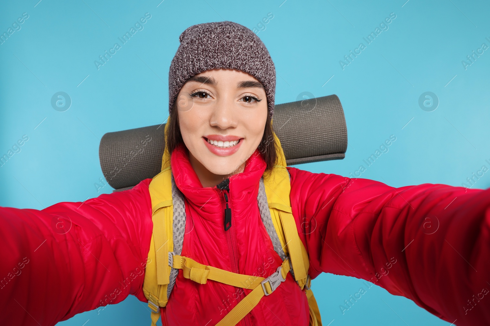 Photo of Smiling young woman with backpack taking selfie on light blue background. Active tourism