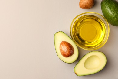 Photo of Cooking oil in bowl and fresh avocados on light grey background, flat lay. Space for text