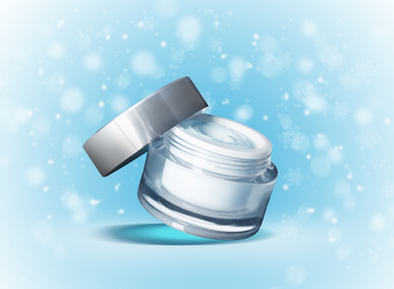 Jar of cosmetic cream on light blue background with blurred snowflakes. Winter skin care