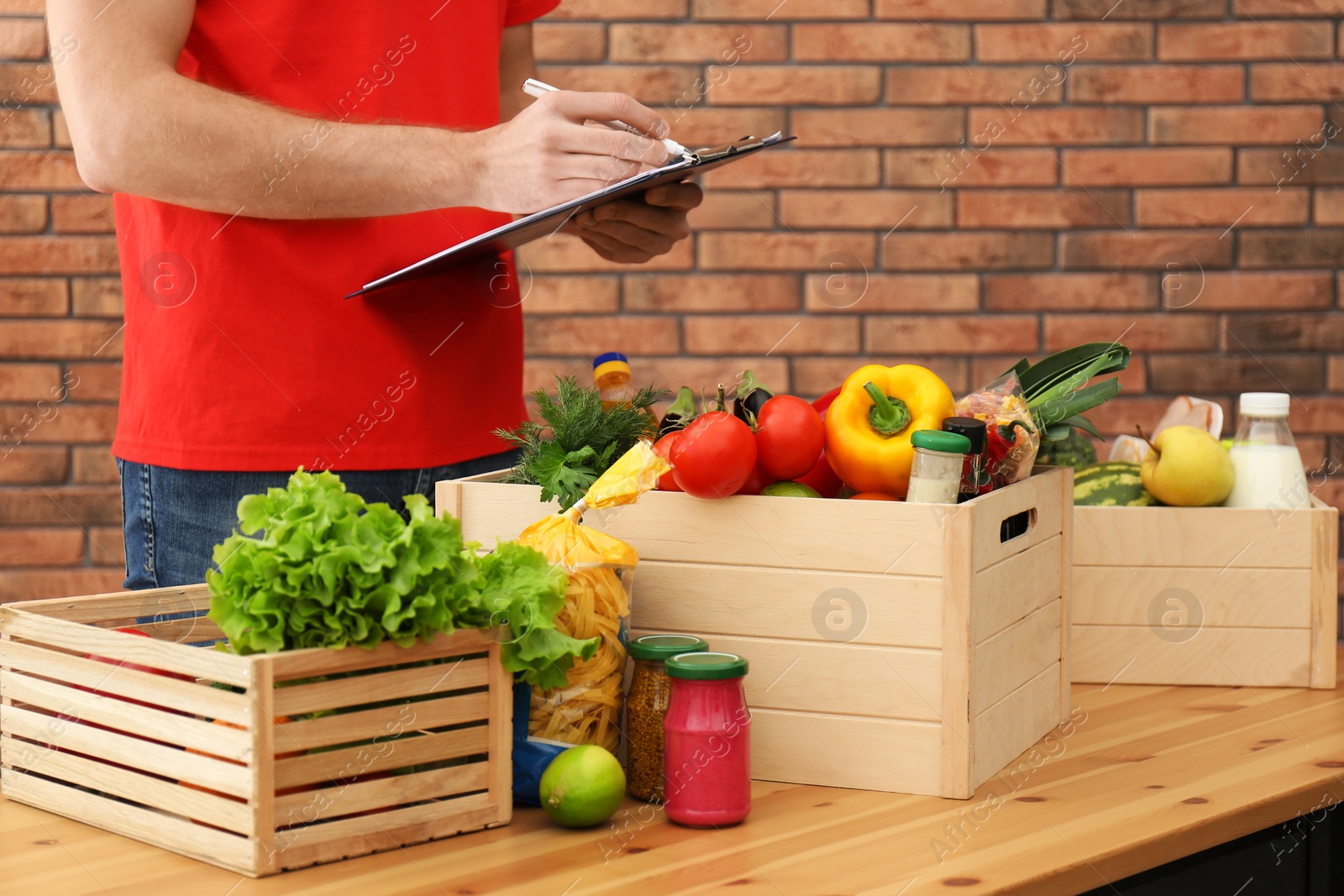 Photo of Man with clipboard and fresh products at table indoors, closeup. Food delivery service