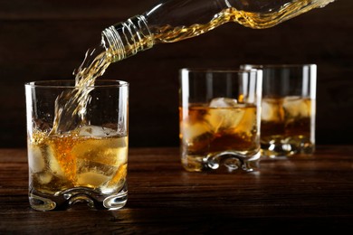 Pouring whiskey from bottle into glass at wooden table, closeup