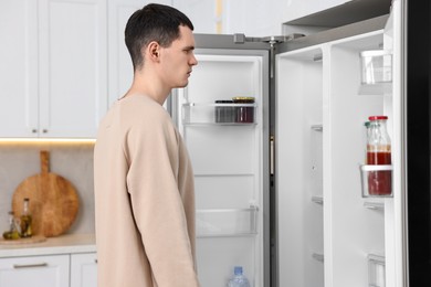Photo of Upset man near empty refrigerator in kitchen