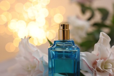 Photo of Bottle of perfume and beautiful lily flowers against beige background with blurred lights, closeup