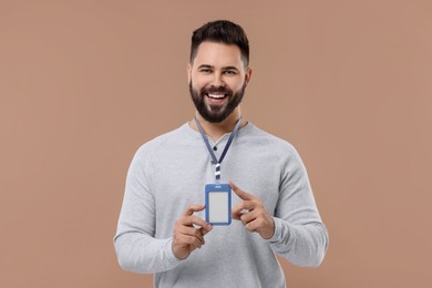 Happy young man with blank badge on beige background