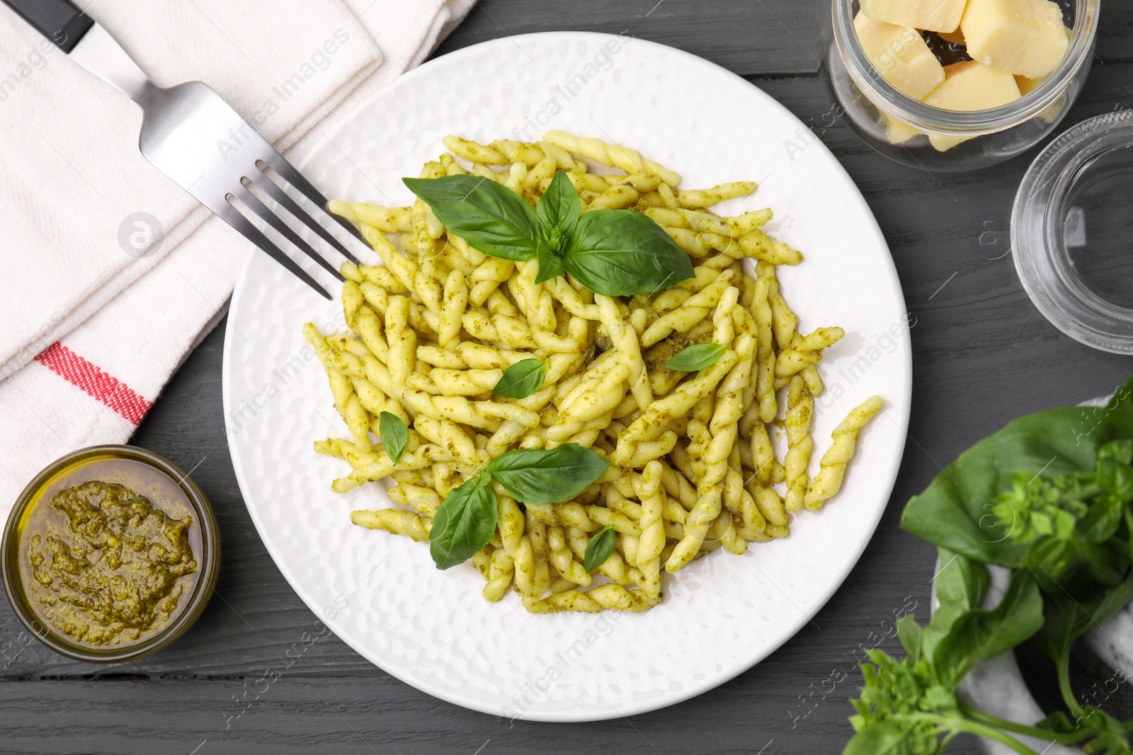 Photo of Plate of delicious trofie pasta with pesto sauce and basil leaves on grey wooden table, flat lay