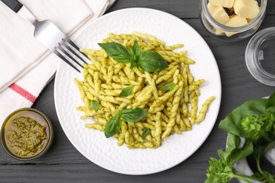 Plate of delicious trofie pasta with pesto sauce and basil leaves on grey wooden table, flat lay