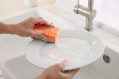 Photo of Woman washing plate above sink in modern kitchen, closeup