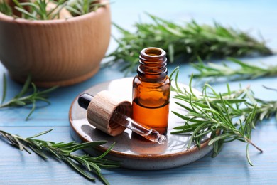 Photo of Bottle of rosemary essential oil and sprigs on light blue wooden table