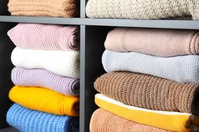 Many knitted winter clothes stacked on shelves, closeup