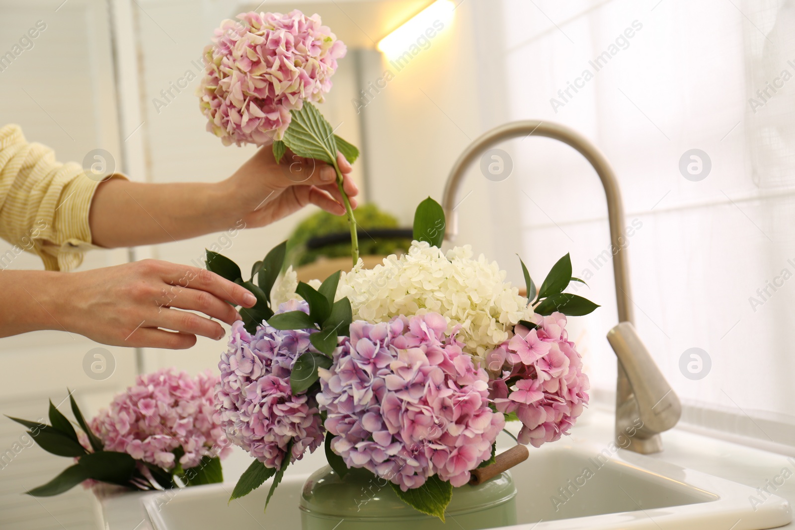 Photo of Woman making bouquet with beautiful hydrangea flowers in kitchen, closeup