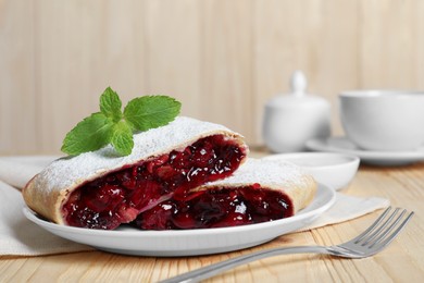 Delicious strudel with cherries, powdered sugar and mint on wooden table, closeup