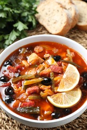 Photo of Meat solyanka soup with sausages, olives and vegetables on wicker mat, closeup