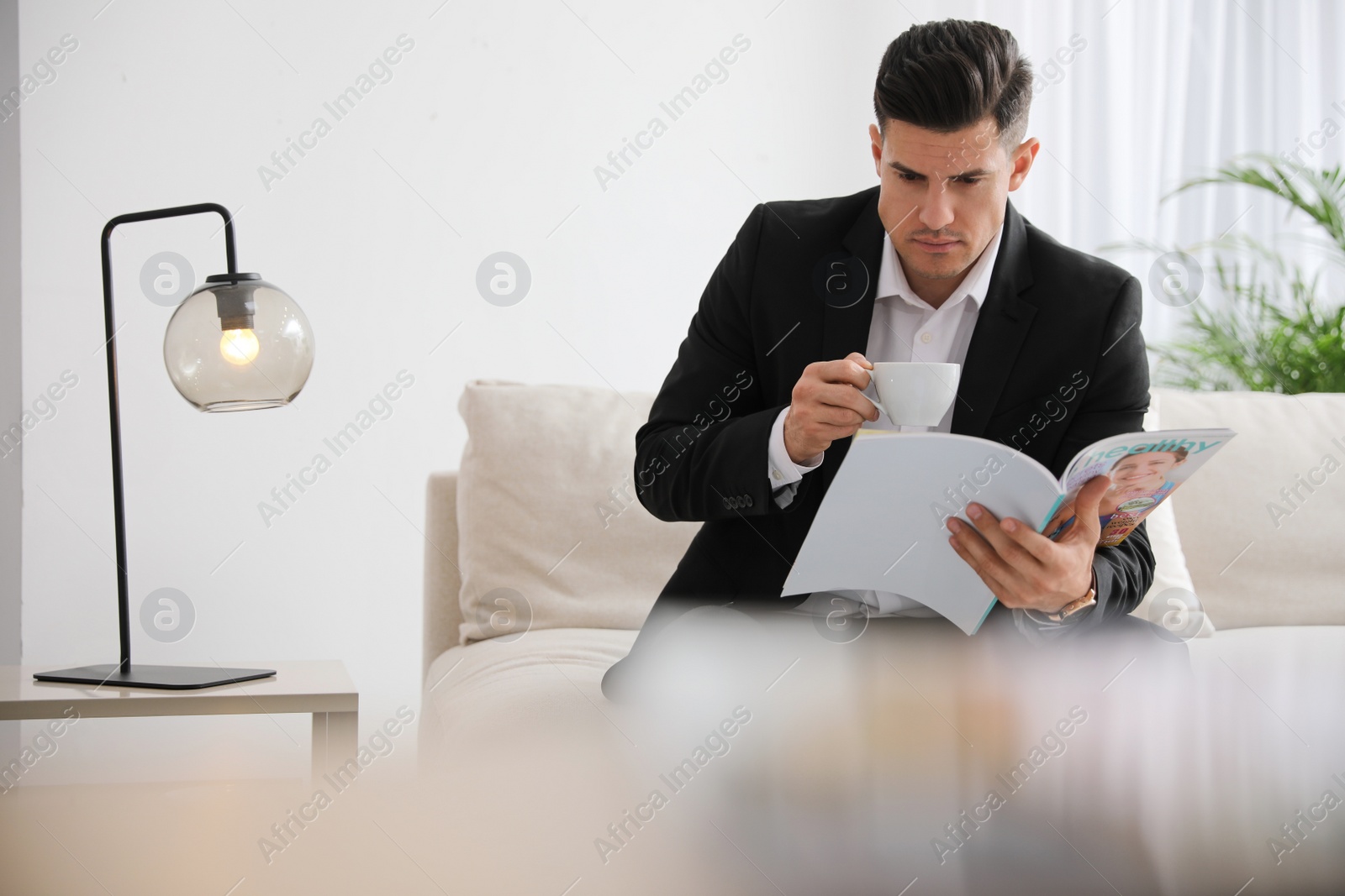 Photo of Man with cup reading magazine on sofa in office