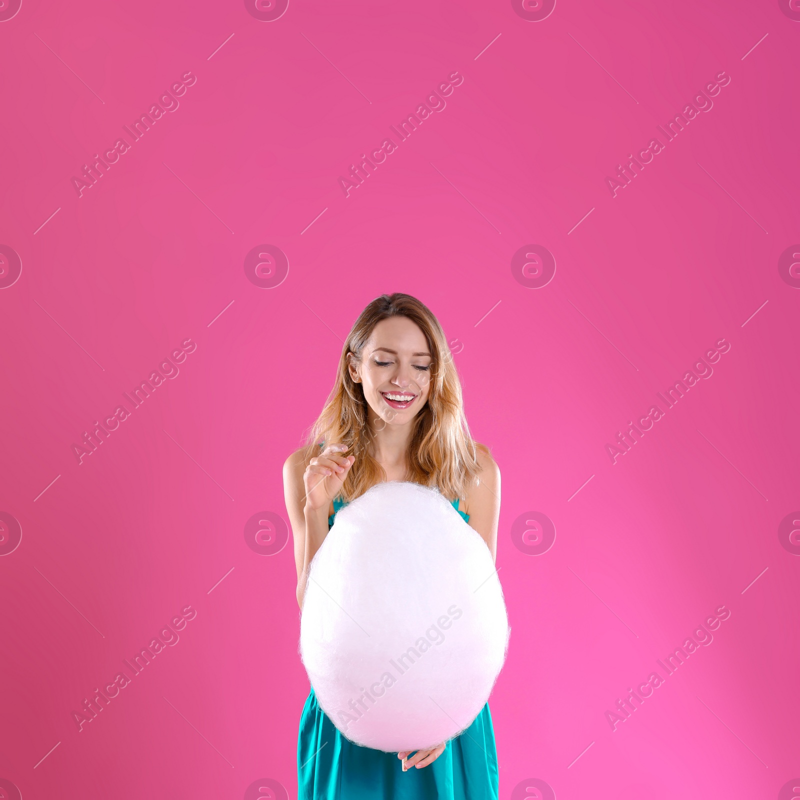 Photo of Happy young woman with cotton candy on pink background