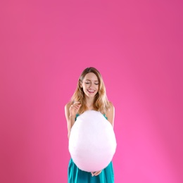 Photo of Happy young woman with cotton candy on pink background