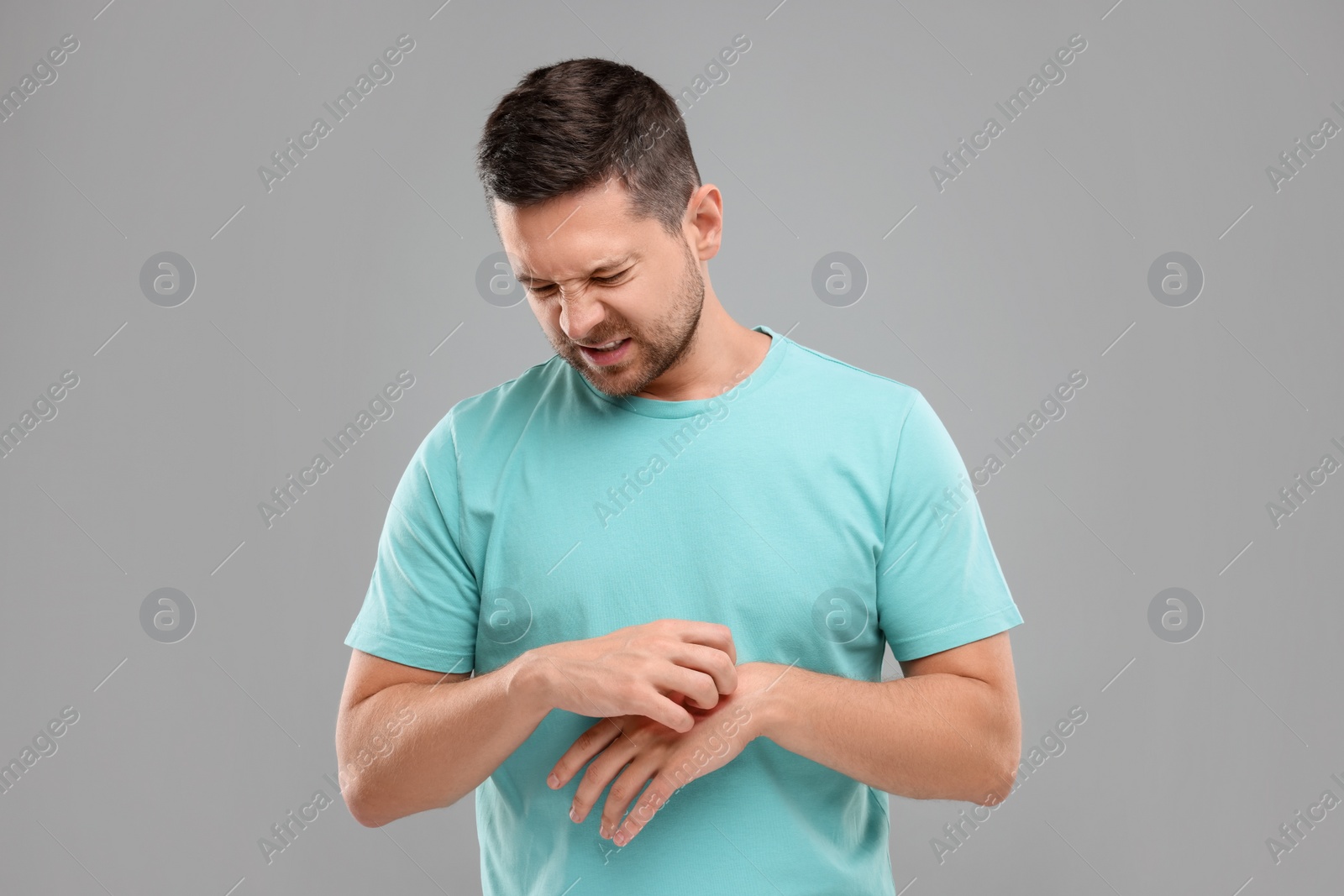 Photo of Allergy symptom. Man scratching his hand on light grey background