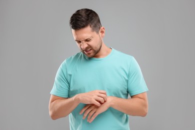 Photo of Allergy symptom. Man scratching his hand on light grey background